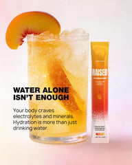 Raised Hydration+ peach on-the-go sachet beside gym bag for travel-ready hydration.
