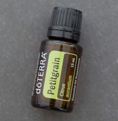 Petitgrain essential oil bottle resting on wood surface for display.