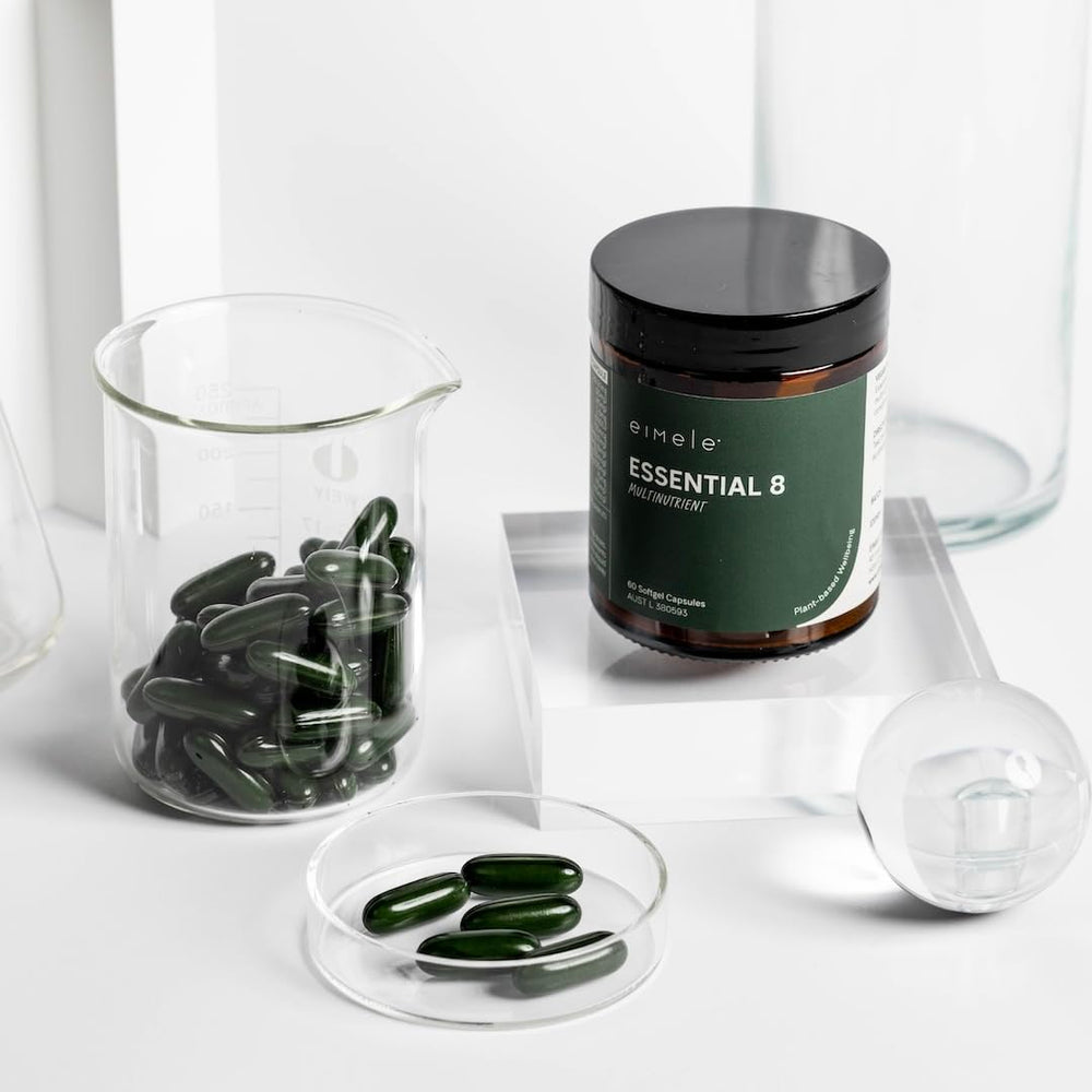 Eimele Essential 8 bottle on wood surface indicating vegan, non-GMO formula.