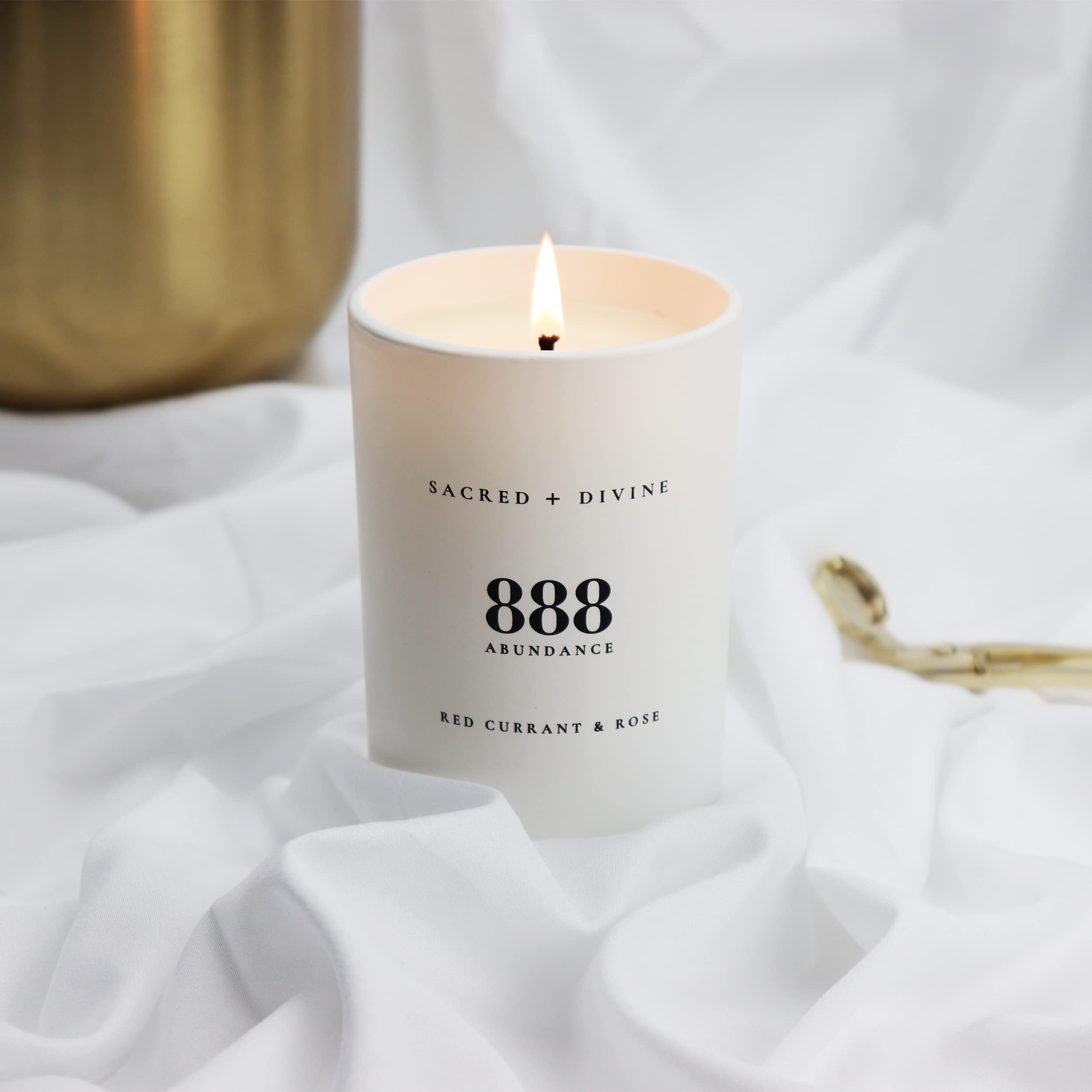 Sacred + Divine 888 abundance candle warm flame creates calming atmosphere.